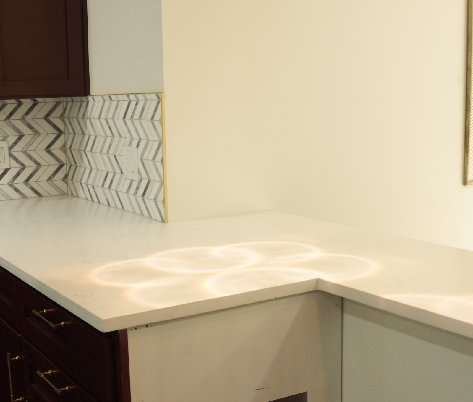 Clean, unmarked white quartz countertop corner beside a chevron tile backsplash